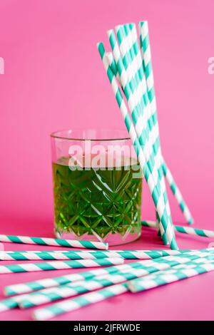 verre à facettes de boisson alcoolisée verte près des pailles en papier à rayures sur le rose Banque D'Images