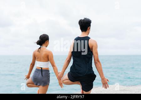 Dos de paisible et conscient asiatique 30s couple appréciant l'arbre pose yoga en bord de mer. Couple de hommes et de femmes est la formation de la méditation et de la spiritualité Banque D'Images