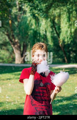 Belle adolescente dans un t-shirt rouge mange des bonbons en coton dans le parc Banque D'Images