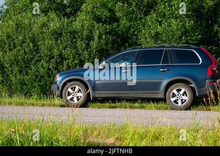 SUV sur le côté d'une route de campagne à côté de buissons verts dans l'herbe verte illuminée par la lumière chaude de coucher de soleil d'été. Banque D'Images