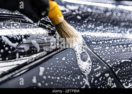 l'employé lave soigneusement une voiture moderne avec une brosse de lavage dédiée Banque D'Images