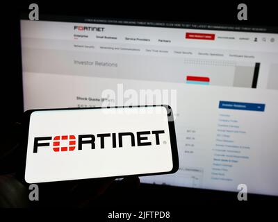 Personne tenant un téléphone portable avec le logo de la société américaine de cybersécurité Fortinet Inc. À l'écran en face de la page Web des affaires. Mise au point sur l'affichage du téléphone. Banque D'Images