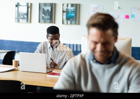 Jeune homme d'affaires afro-américain souriant travaillant sur un ordinateur portable dans un bureau créatif Banque D'Images