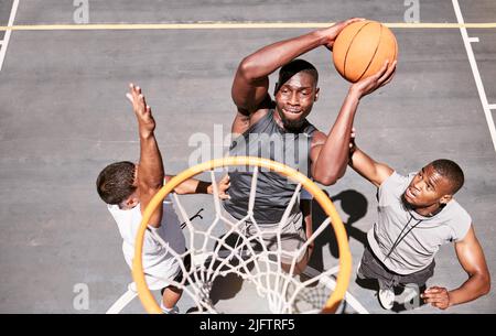 Les joueurs de basket-ball bloquant un joueur de dounking d'une balle dans le filet pour marquer des points pendant un match sur un terrain de sport d'en haut . Des athlètes qui sautent Banque D'Images