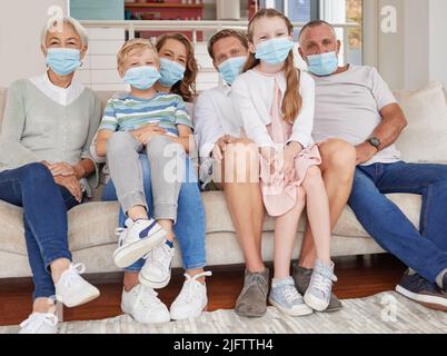Portrait d'une famille caucasienne de génération heureuse portant des masques tout en se relaxant sur un canapé à la maison. Les enfants, les parents et les grands-parents restent responsables Banque D'Images