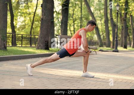 Sportsman tenir la position de fente faire une routine d'étirement pendant l'entraînement sportif en plein air dans le parc, l'échauffement Banque D'Images