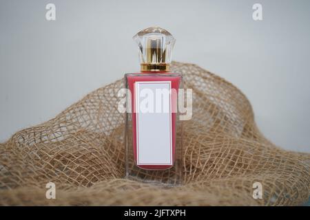 Bouteille de parfum rouge avec rectangle blanc et capuchon doré, sur fond blanc et parfum de toile de jute maquette. Et 3D rendu Banque D'Images