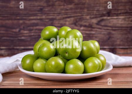 Prune verte sur fond de bois. Pile de prunes vertes sur une assiette de service blanche. Gros plan Banque D'Images