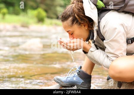 Profil d'une eau potable de trekker directement de la rivière avec des mains en forme de bute dans la montagne Banque D'Images