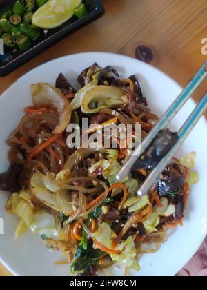 Japchae avec des carottes et des graines de sésame dans la plaque blanche sur la table.est un plat salé et légèrement sucré de nouilles de verre sautées et de légumes. Banque D'Images
