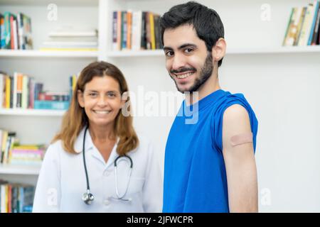 Rire de l'homme arabe après la troisième vaccination contre Covid 19 avec une infirmière à l'hôpital Banque D'Images