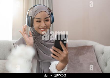 Femme musulmane assise sur un canapé et vidéoconférence sur un téléphone portable. Femme asiatique musulmane appel vidéo. Banque D'Images