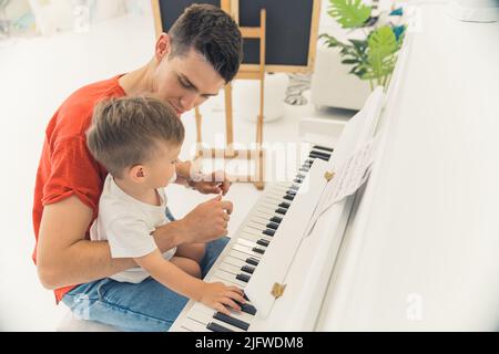 jeune père enseignant à son petit fils comment jouer du piano, plan moyen. Photo de haute qualité Banque D'Images