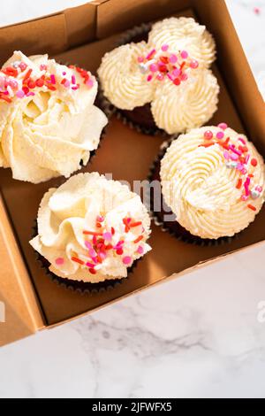 Emballage des petits gâteaux en velours rouge fraîchement cuits avec ganache au chocolat blanc dans la boîte à petits gâteaux. Banque D'Images