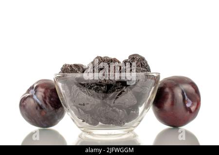 Deux prunes noires fraîches mûres et quelques prunes dans un bol en verre, en gros plan, isolées sur fond blanc. Banque D'Images