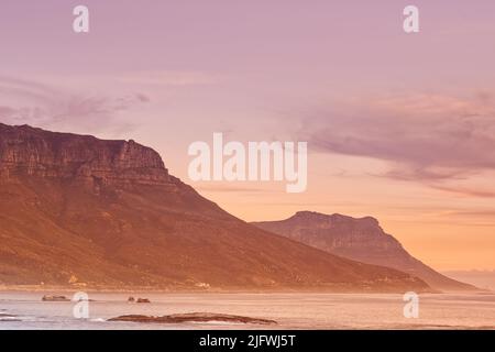 Une montagne et le bord de mer contre le ciel et le coucher de soleil copyspace arrière-plan. Vue panoramique sur l'océan au lever du soleil avec espace de copie, port de Hout Bay avec vue sur l'océan Banque D'Images