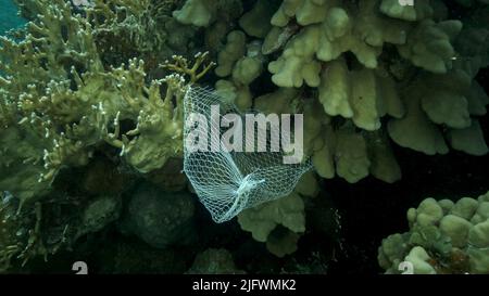 Les articles de cuisine en plastique mis au rebut pendent du récif de corail. Pollution plastique de l'océan. Sac en plastique en maille accroché à un magnifique corail Banque D'Images