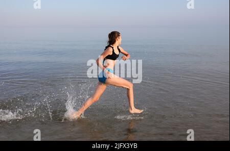 une jeune fille sportive court rapidement sur l'eau au bord de la mer pendant l'entraînement quotidien Banque D'Images