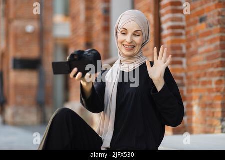 Jeune femme musulmane utilisant une caméra vidéo pour enregistrer de la vidéo pour son travail. Heureuse et excitée femme d'affaires arabe porte des vêtements noirs avec hijab, en signe d'attirer le public d'Internet. Concept de vlogging d'influenceur Banque D'Images