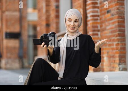 Jeune femme musulmane utilisant une caméra vidéo pour enregistrer de la vidéo pour son travail. Heureuse et excitée femme d'affaires arabe porte des vêtements noirs avec hijab, en signe d'attirer le public d'Internet. Concept de vlogging d'influenceur Banque D'Images