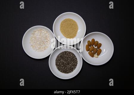 Amandes, chia et autres graines végétaliennes saines dans 4 bols ronds en porcelaine blanche sur fond noir Banque D'Images