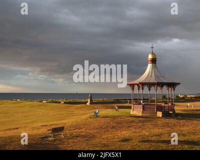 Vue sur Nairn Links pendant une soirée d'été. La lumière rouge teintée sur l'herbe, et la métallurgie du Wallace Bandstand contre les nuages de pluie. Banque D'Images