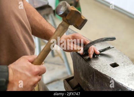 D'en haut anonyme homme frapper la chaussure de cheval en fer avec un marteau sur l'enclume tout en travaillant dans l'atelier sur le ranch Banque D'Images