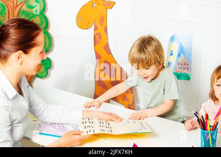 Adulte enseigne aux petits enfants à lire des lettres dans le livre Banque D'Images