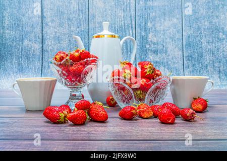 Les fraises mûres rouges se trouvent dans deux vases en cristal et sur une table en bois. Une cafetière et deux tasses sont côte à côte. Banque D'Images