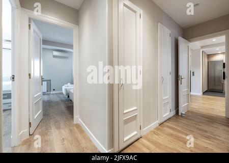 couloir d'une maison avec boiseries blanches et parquet clair avec accès à plusieurs chambres Banque D'Images