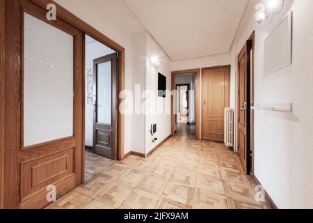 Entrée et couloir d'une maison avec parquet en chêne usé, menuiserie de porte du même matériau et accès à plusieurs chambres Banque D'Images