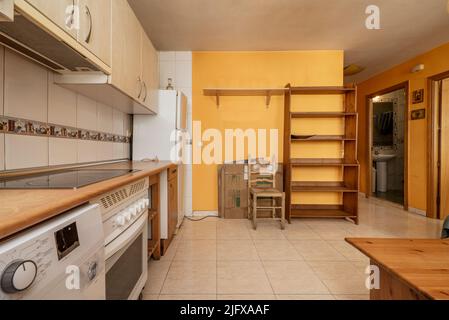 Façade de cuisine avec armoires en merisier en dessous et armoires lumineuses au-dessus avec appareils électroménagers blancs intégrés, murs carrelés et peints en jaune Banque D'Images