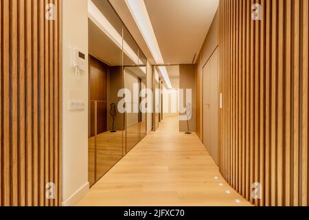 Couloir d'une maison avec un mur recouvert de miroirs d'un côté et de lattes en bois de l'autre, parquet en châtaignier et lumières encastrées dans le sol Banque D'Images