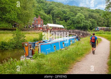 Un homme qui marche le long du canal narrowboat amarré sur le canal Caldon devant le pub Black Lion à Consall Wharf dans la vallée de Churnet Staffordshire Angleterre Banque D'Images