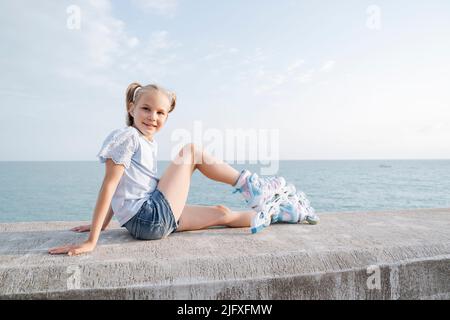 Une fille en patins à roulettes est assise sur la mer. Banque D'Images