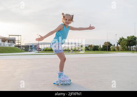 Une fille patine dans le parc sur des patins à roulettes au coucher du soleil. Banque D'Images