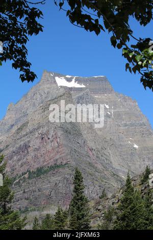 Rochers colorés de Going-to-the-Sun Mountain, vue est, encadrés par des feuilles vertes, des pins verts, ciel bleu brillant. Parc national des Glaciers, Montana, États-Unis Banque D'Images