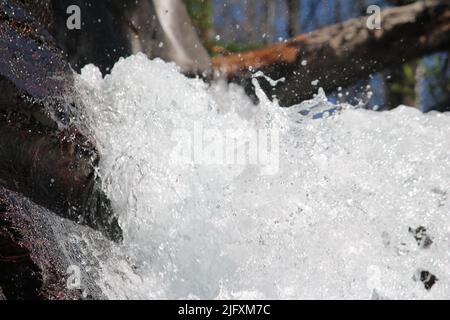 Vue rapprochée immersive d'une eau en cascade et pétillante qui coule sous le bois et au-dessus de la falaise rouge, des chutes de Baring, du parc national de Glacier, du Montana, des États-Unis Banque D'Images