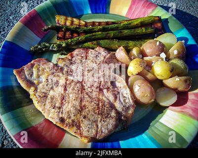 Repas authentique d'été repas de pique-nique maison au barbecue composé de côtelettes de porc, pommes de terre à l'ail, asperges grillées et aubergines grillées. Banque D'Images