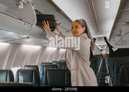 Femme asiatique voyageur mettant des bagages dans un casier à bagages à bord d'un avion pendant l'embarquement Banque D'Images