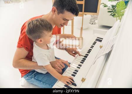 petit garçon jouant le paino avec son père, plan moyen en intérieur, concept familial. Photo de haute qualité Banque D'Images