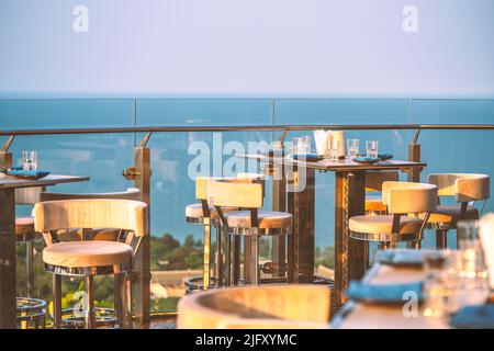 Restaurant extérieur élégant et luxueux sur le toit d'un bâtiment, ustensiles sont mis sur la table, clôture en verre, fond flou du ciel et de la mer, la veille Banque D'Images