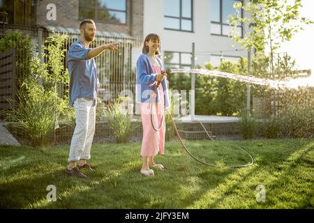 Beau couple arroser la pelouse à l'arrière-cour Banque D'Images