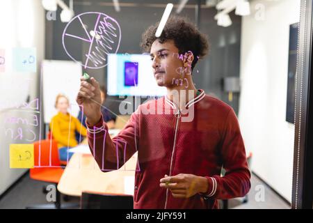 Carte de dessin de développeur d'applications pour jeunes biraciaux mâles sur verre dans la salle de bord Banque D'Images