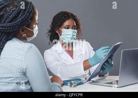 Femme afro-américaine médecin en cabinet médical avec un patient tout en portant un masque de protection pendant un rendez-vous médical Banque D'Images