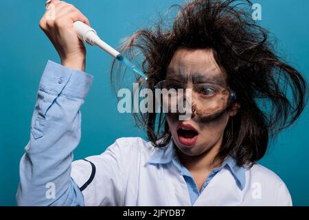 Chimiste lunatique regardant choqué par la pipette professionnelle remplie de substance liquide expérimentale. Insensée, la chimie folle réréearcher avec le visage sale et les cheveux désordonnés expérimentant avec des composés inconnus. Banque D'Images