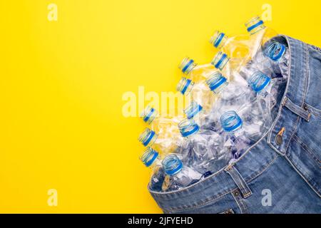 Recyclez la technologie de la bouteille en plastique pour fabriquer des vêtements. Vue de dessus une vieille bouteille d'eau et un Jean court bleu sur fond jaune Banque D'Images