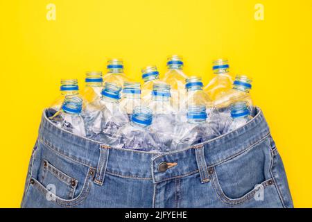 Recyclez la technologie de la bouteille en plastique pour fabriquer des vêtements. Vue de dessus une vieille bouteille d'eau et un Jean court bleu sur fond jaune Banque D'Images