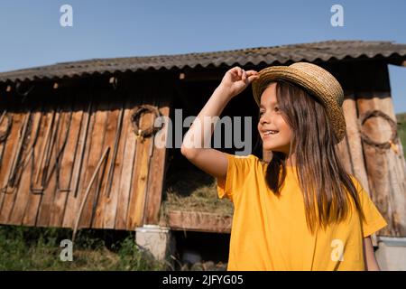 bonne fille en chapeau de paille regardant loin près de la grange en bois sur la ferme du village Banque D'Images