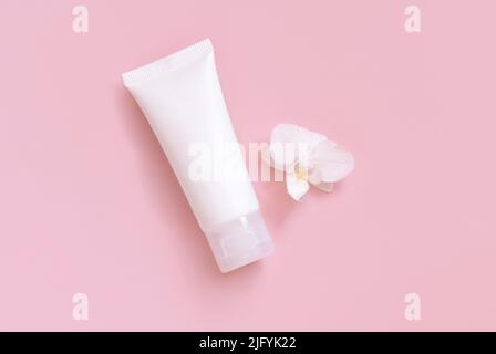 Tube de crème en plastique blanc près de la fleur d'orchidée blanche sur jaune clair, vue de dessus, maquette. Produit de beauté, crème ou lotion pour les soins de la peau. Cosmétique exotique naturelle Banque D'Images